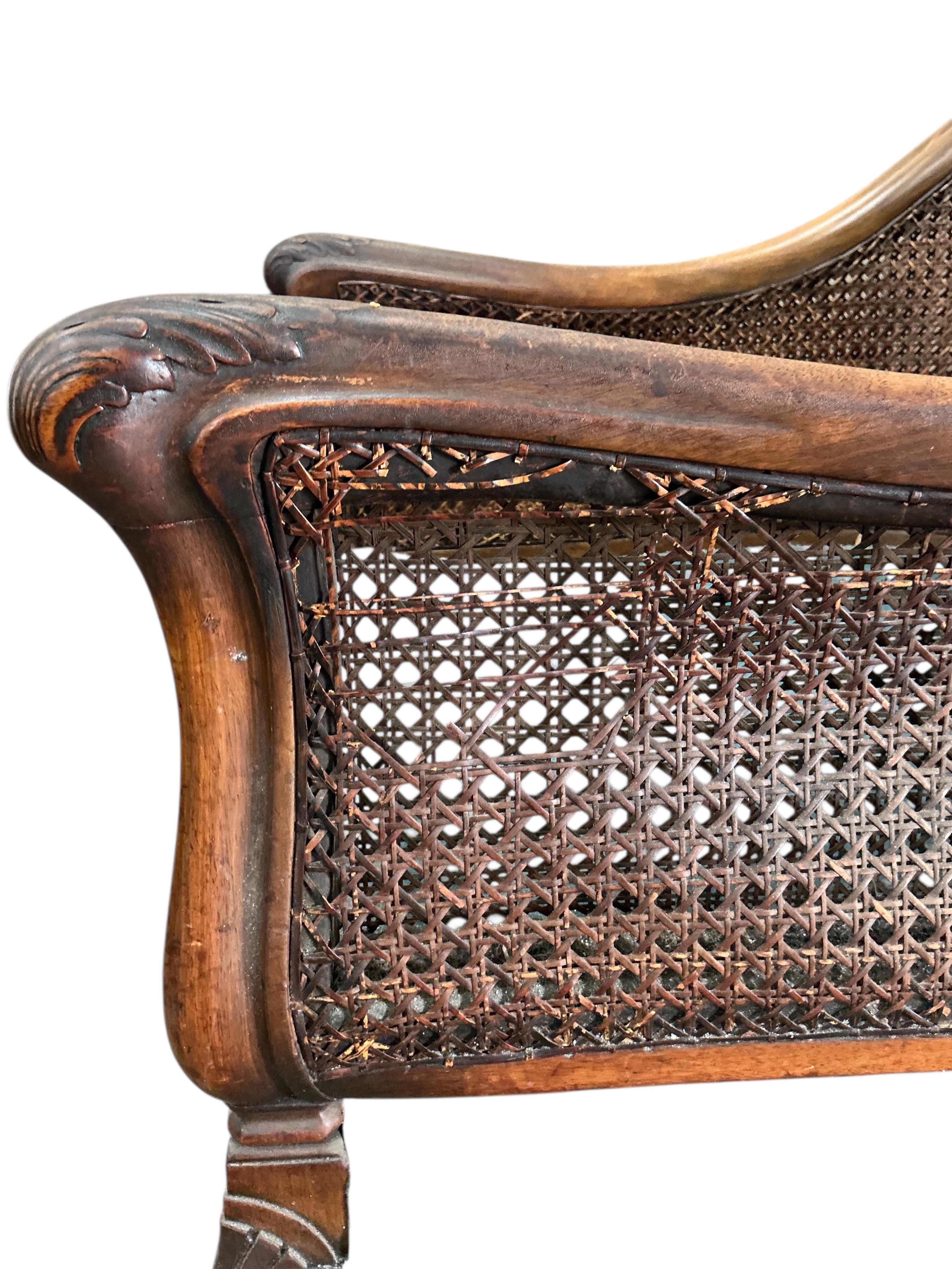 An early 20th century carved walnut and double canework three piece bergère suite, cane in need of repair